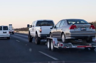 Truck towing a grey car on the highway